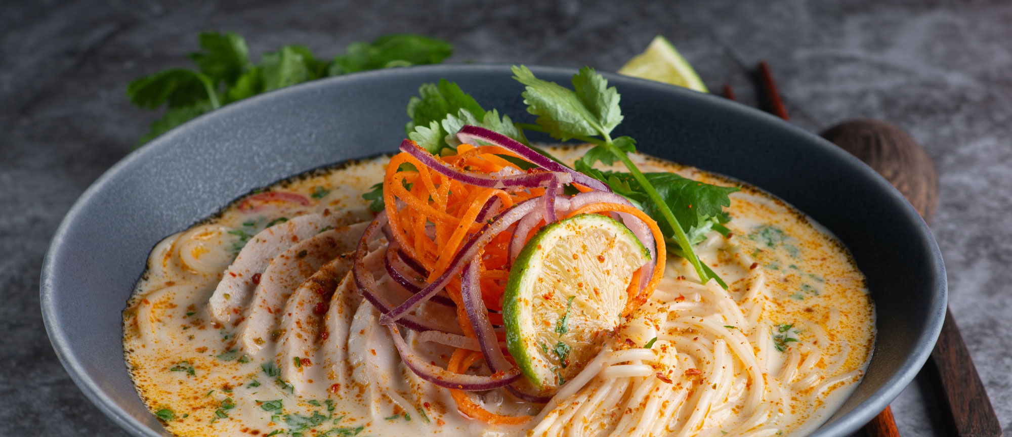 Noodle soup garnished with lime, carrots, onions and coriander leaves.