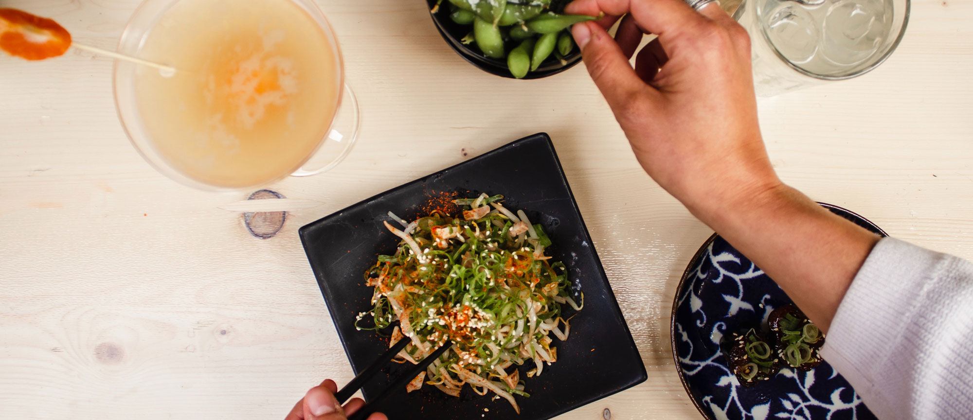 Plats vegan, dont des édamames servis dans des assiettes noires,accompagnés de boissons.