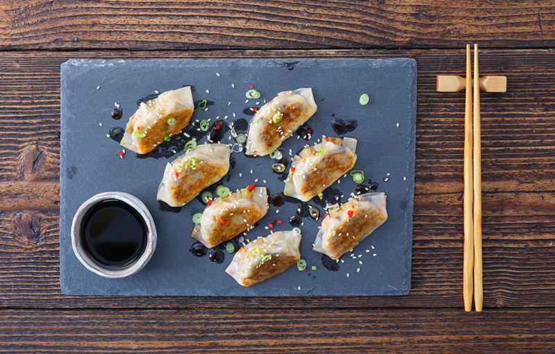 Dumplings servis avec de la sauce soja, sur un plateau noir avec des baguettes.