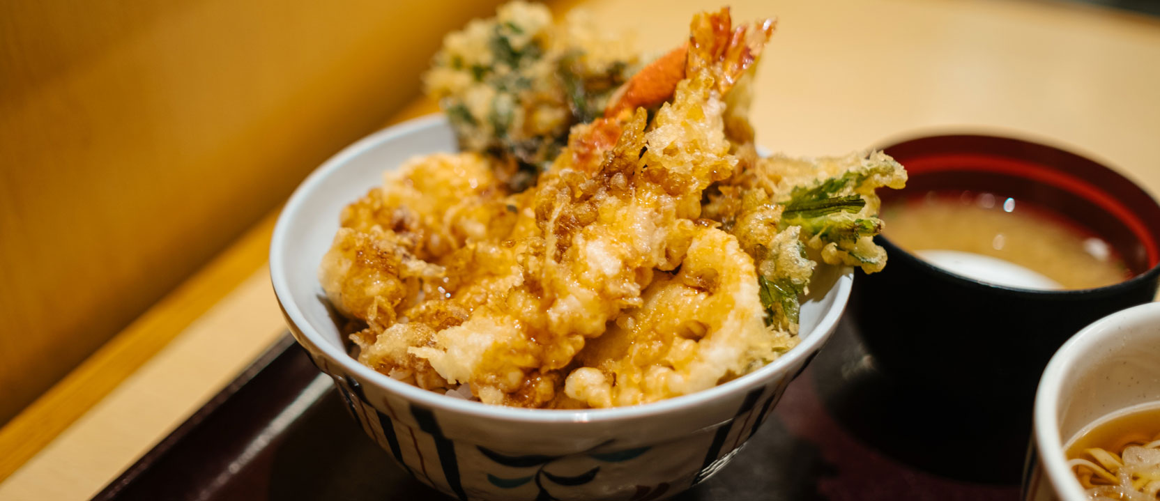 Tempura served in a bowl, on a brown tray, alongside dipping sauces.